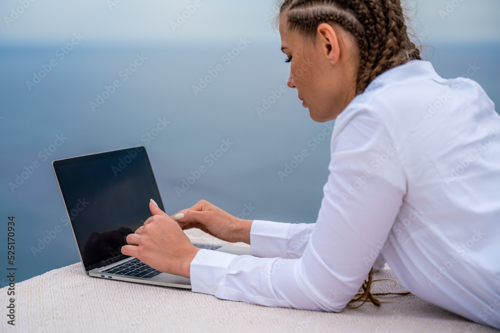 A woman is typing on a laptop keyboard on a terrace with a beautiful sea view. Close up of a woman's hands writing on a computer. Freelancing, digital nomad, travel and vacation concept. A woman is typing on a laptop keyboard on a terrace with a beautiful sea view. Close up of a woman's hands writing on a computer. Freelancing, digital nomad, travel and vacation concept.