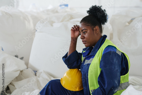 Young tired female engineer or worker of warehouse sitting by heap of huge white sacks with raw materials and having rest after work