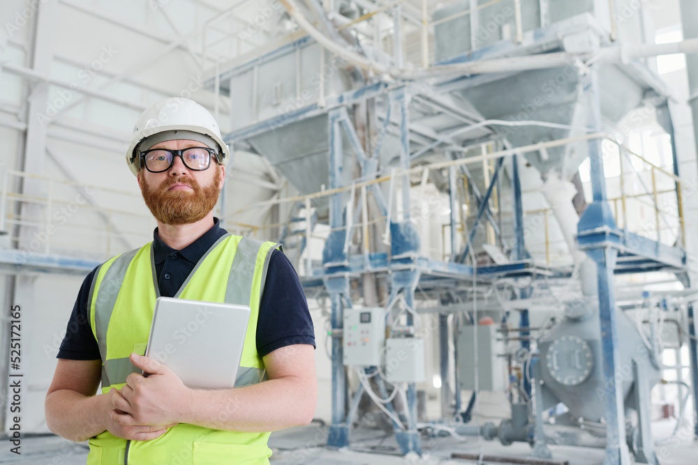 Young confident engineer or technician of modern production factory in workwear, eyeglasses and protective helmet looking at camera Young confident engineer or technician of modern production factory in workwear, eyeglasses and protective helmet looking at camera