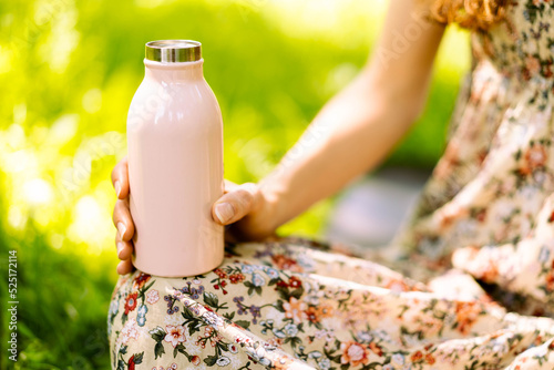 Close-up of steel eco thermo water bottle in female hand. Green background in the park. Copy space concept. Space for text. Plastic free. Zero waste concept. Selective focus. 