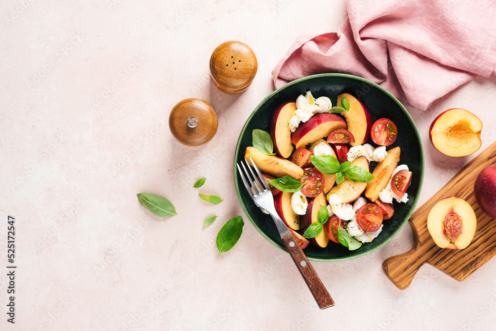 Salad with peach, mozzarella cheese and tomatoes on green plate, pink background with copy space. Top view. Healthy vegetarian summer fruit and cheese salad
