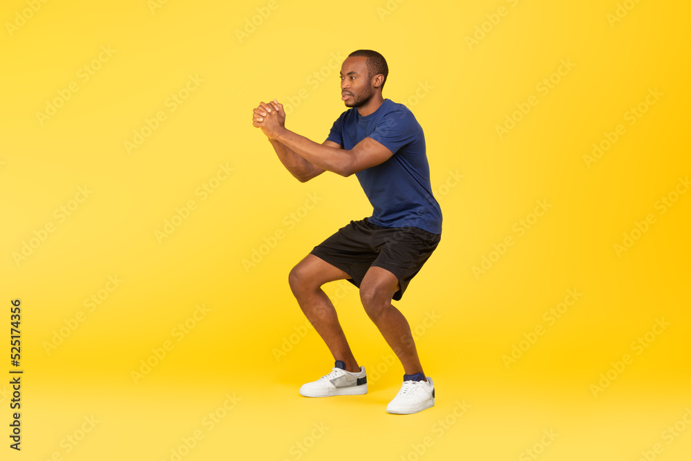 Athletic African American Man Doing Deep Squat Exercise, Yellow Background