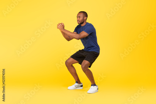 Athletic African American Man Doing Deep Squat Exercise, Yellow Background © Prostock-studio