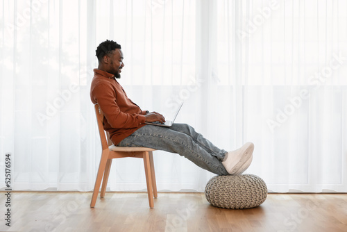 Black Man Using Laptop Working Online At Home, Side View