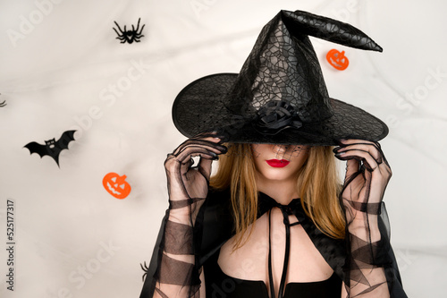 Halloween Witch . Beautiful youn blonde with red lips covertin her eyes with hat. Selective focus on the hat