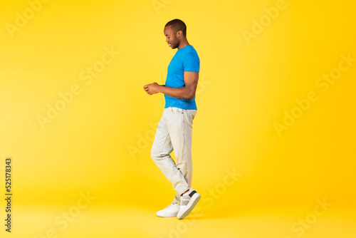 Black Male Using Cellphone Texting Standing Over Yellow Studio Background