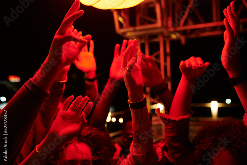 Raised hands of young energetic friends dancing at rooftop party in outdoor cafe at night time and enjoying their gathering
