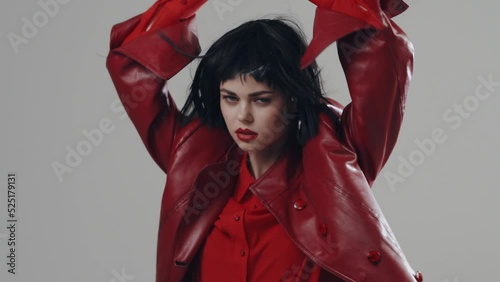 A beautiful woman model poses in a red cape in front of the camera in a black wig and with red lips. Professional shooting of model fashion posing