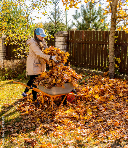 Young Woman having fun throwing while cleaning fallen maple autumn leaves in the garden.