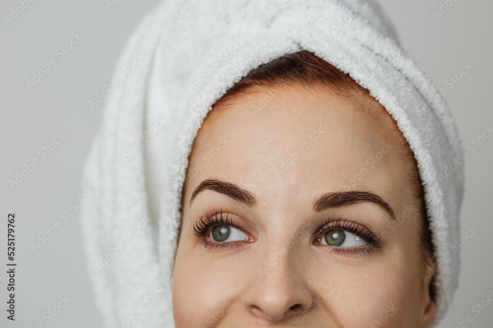 Obraz premium Focuse un eyes. Close up portrait of pleasant young woman in towel isolated over grey studio background. Concept of skincare and beauty.
