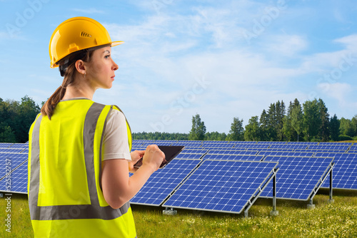 Solar energy technologies. Solar power plant engineer. Woman with tablet in yellow vest. Eco power plant construction concept. Green energy. Solar panels on grass. Getting electricity from sunlight