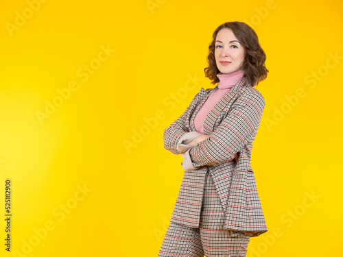 Successful woman. Girl crossed her arms. Successful woman in plaid suit. Business girl stands on yellow background. Lady with brown long hair. Successful female manager. Portrait woman.