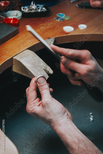 Delicate jewelry work. Close up of a male jeweler working and shaping an unfinished ring with a tool in workshop