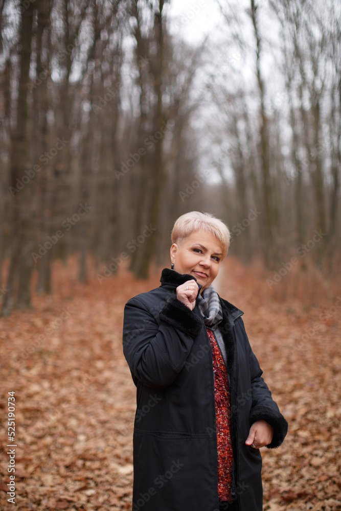 Middle age woman with stylish short haircut in black coat in autumn forest. Middle age woman with stylish short haircut in black coat in autumn forest.