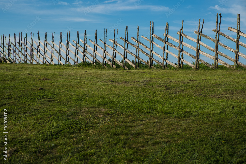 Handmade old wooden fence with green grass land and blue sky. Summer country style background.