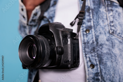 Close up shot of photography enthusiast wearing fashion denim jacket while having modern DSLR camera. Professional photographer having photo device while standing on blue background.