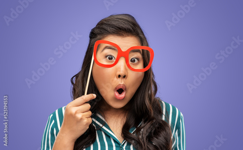 party props, photo booth and people concept - happy woman with big glasses making faces over violet background