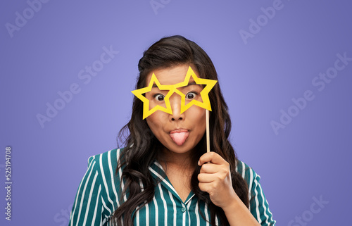party props, photo booth and people concept - happy woman with big glasses in shape of stars sticking out her tongue over violet background