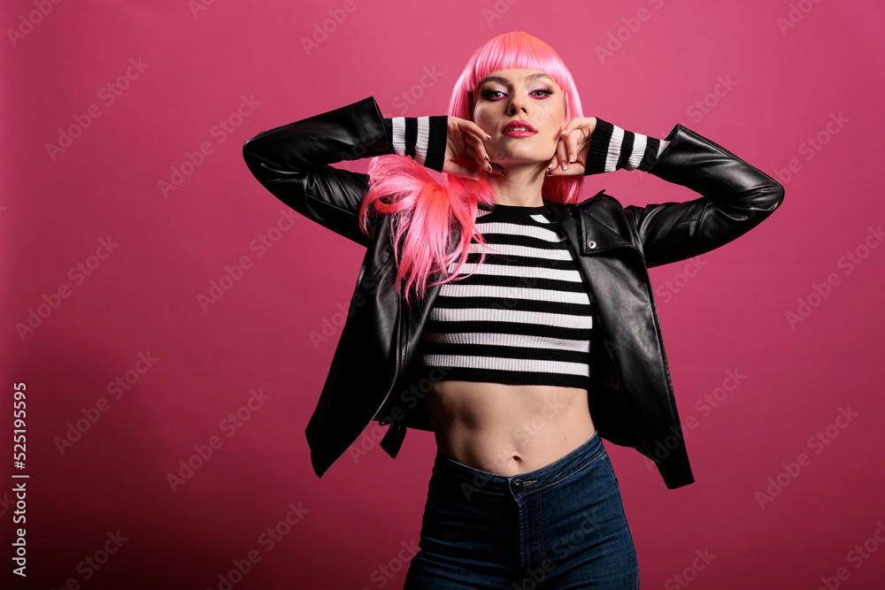 Beautiful sensual woman with pink hair wearing punk leather jacket to be trendy and advertise rocker fashion style. Female model feeling funky and attractive, standing over studio background.