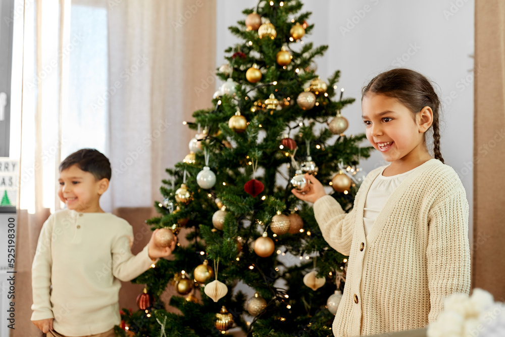 x-mas, winter holidays and childhood concept - happy smiling little girl and boy decorating christmas tree at home x-mas, winter holidays and childhood concept - happy smiling little girl and boy decorating christmas tree at home