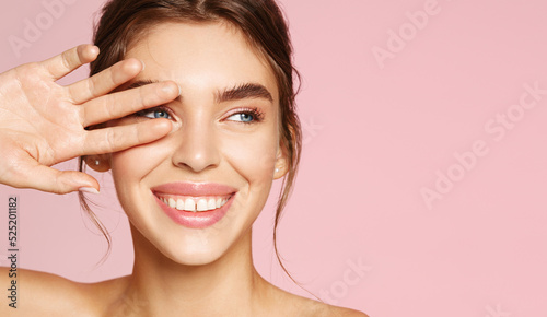 Skin care. Woman with beauty face touching healthy facial skin portrait. Beautiful smiling girl model with natural makeup touching glowing hydrated skin on pink background closeup