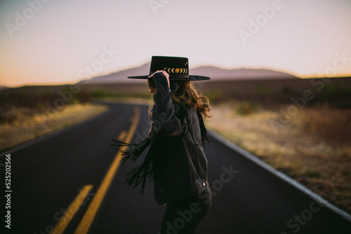 Woman in hat and fringe jacket dancing in the street in the desert at sunset photo