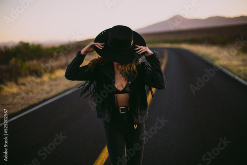 Woman in hat and fringe jacket dancing in the street in the desert at sunset photo
