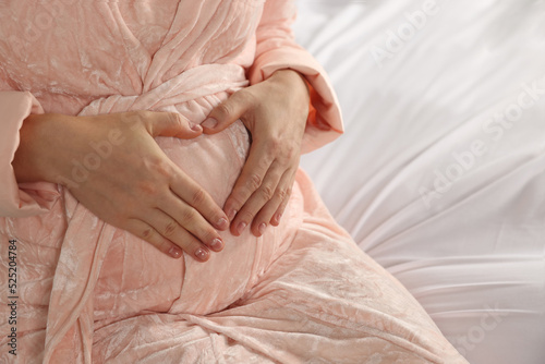Pregnant woman in bathrobe on bed, closeup