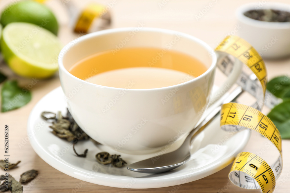 Cup of diet herbal tea, measuring tape and dried leaves on table, closeup Cup of diet herbal tea, measuring tape and dried leaves on table, closeup