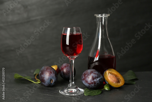 Delicious plum liquor and ripe fruits on black table. Homemade strong alcoholic beverage photo