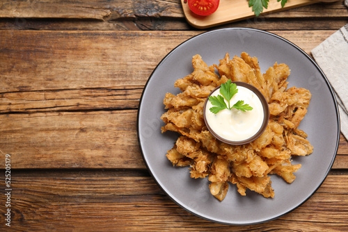 Fried blooming onion with dipping sauce served on wooden table, flat lay. Space for text