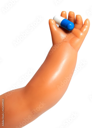 Baby doll arm and hand holding medication capsule.