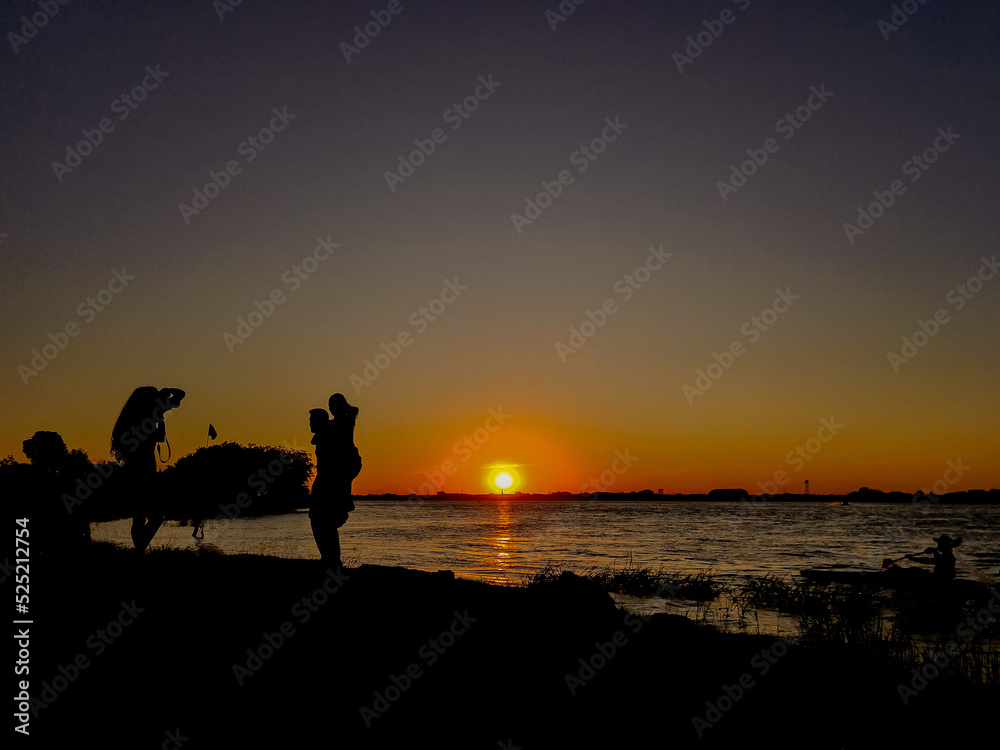 Silhouette of people being photographed at sunset on a river
