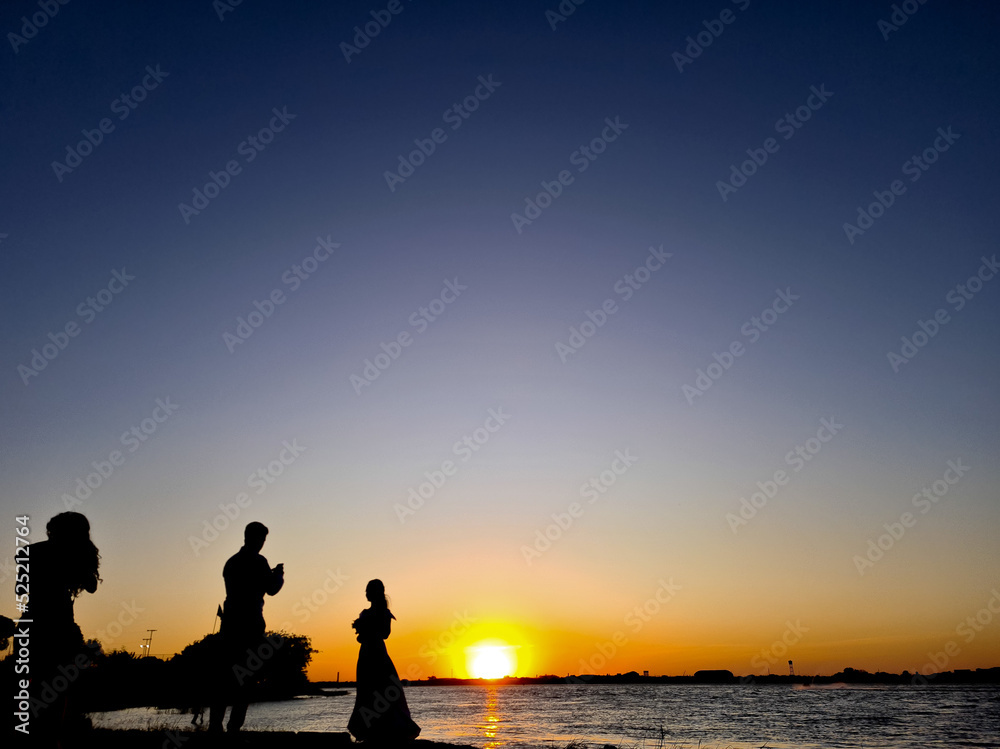 Silhouette of people being photographed at sunset on a river