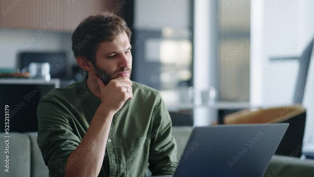 pensive man is working with laptop at home at evening, writing message in online chat and working on book. Business man laptop touches chin thinks over strategy work remotely from home, creative job