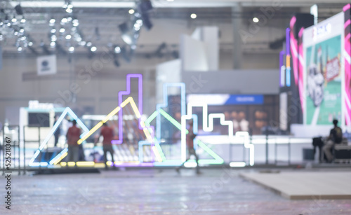 Blurry workers preparing exhibition event hall. Bokeh background of trade show business, world or international expo showcase, tech fair, with exhibitor trade show booth displaying product. photo