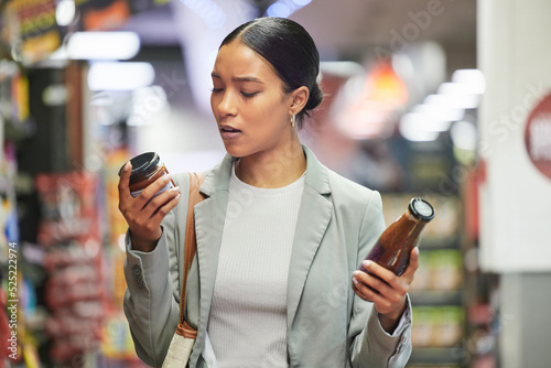 Shopping, retail and customer in a store or supermarket, reading product labels of choice to decide or compare sauce bottles. Consumerism, spending and shopping for food, groceries and a sale offer photo