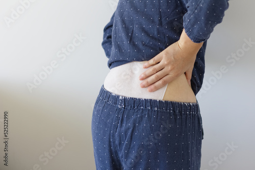 Foto 湿布を貼った腰に手をあてる女性の後ろ姿
