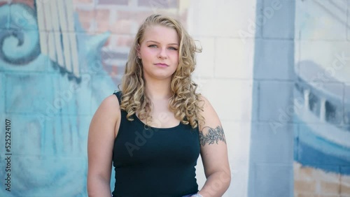 Girl with tattoos crosses her arms and looks at the camera in front of a creative mural. Slow motion. photo