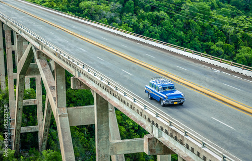 A blue car is driving on the bridge that crosses jungles