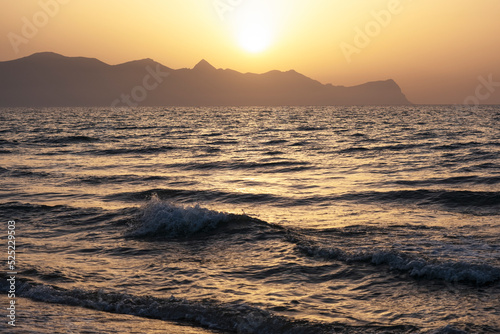 Sunset on island of Sicily, Italy.Waves against the background of the setting sun. Silhouette of mountains in background. Relax, evening on vacation.