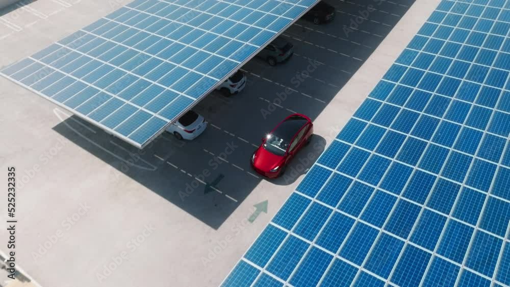 Aerial red electric car on rooftop parking with solar panels. Zero pollution car, green energy concept on modern rooftop parking lot. Alternative energy for ecological cars under blue solar batteries