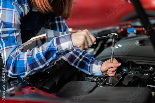 Female auto mechanic unscrewing a nut to replace a car spark plug.
