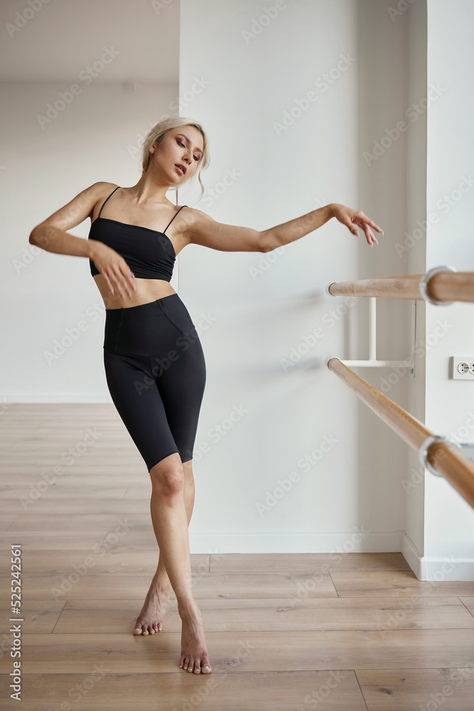 A beautiful girl is engaged in choreography. Doing a warm-up in a black tight-fitting suit. Dancing at the ballet barre