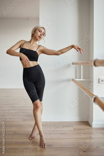 A beautiful girl is engaged in choreography. Doing a warm-up in a black tight-fitting suit. Dancing at the ballet barre