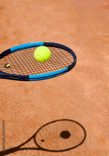 The head of a tennis racket with a yellow tennis ball. The shadow of the racket on the ground. Racket strings. Stretch. Copy space for text. Sports themes. Backgrounds. © LKoroleva
