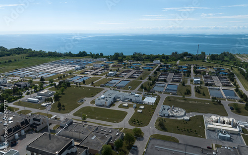 An aerial view above a vast, waterfront water treatment plant, seen during the day.