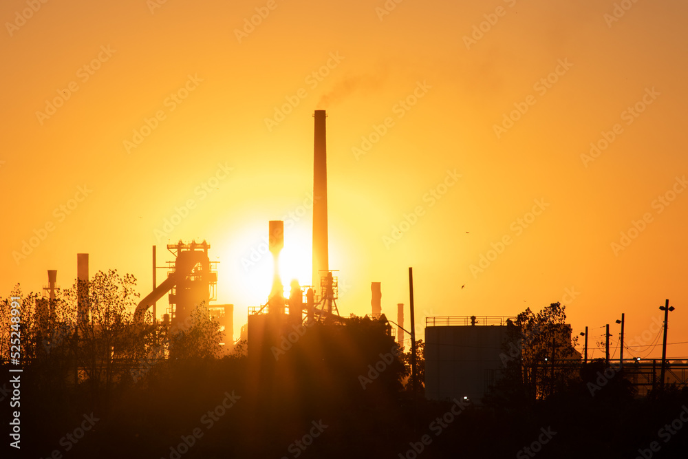 The evening sun shines an industrial smokestack, large factory facility at dusk.