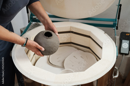close-up of hands putting vase into the kiln, oven for roasting of unbaked clay handmade products, Unfinished ceramics and utensil. Modern pottery oven ready for firing. photo