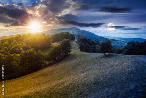 green pasture on the hillside at twilight. day and night time change concept. forested mountains in the distance. beautiful countryside landscape of transcarpathia in summer with sun and moon